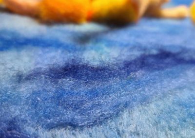 Still using a light touch and loose felting, begin adding another wave in a darker shade directly next to the mid-tone shade of blue.