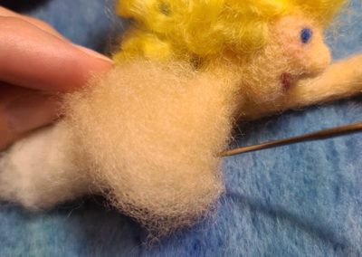 Attach the flesh tone wool over the shoulders by first securing the wool in place along the back front shoulder, which is also helping to secure the neck and head more firmly in place.