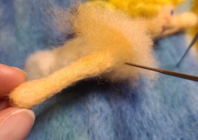 Covering the shoulders with flesh tone wool will provide the fibers necessary to wrap around the end of the arm and attach it to the body.