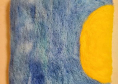 Once the blue wool is covering the remainder of the base, continue adding more yellow wool to build up the ball of the sun.